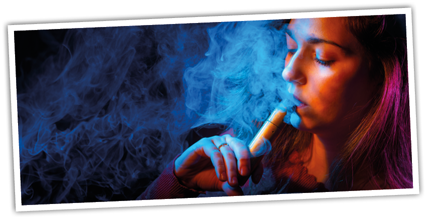 A person with shoulder-length hair is holding and inhaling from a vape device surrounded by colorful blue and orange smoke. Description generated by AI