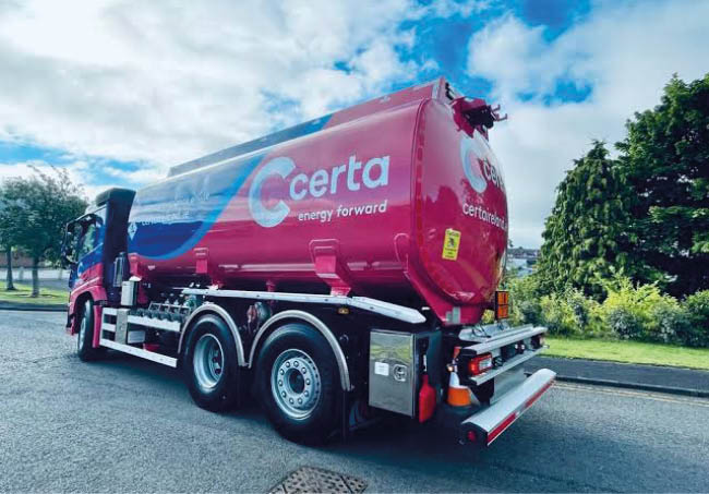 A red and blue fuel tanker truck with the logo “certa energy forward" is parked on a paved surface under a partly cloudy sky. Description generated by AI