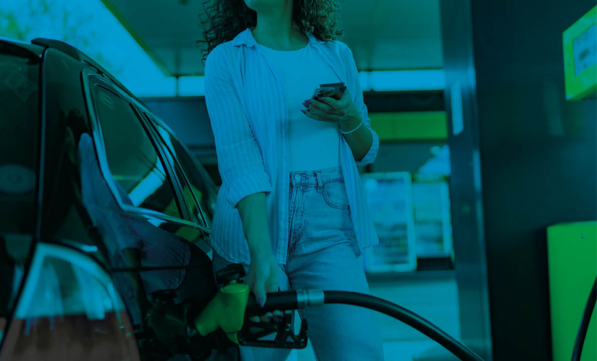 A young beautiful woman does not follow the safety rules and uses the phone while filling her car gas tank