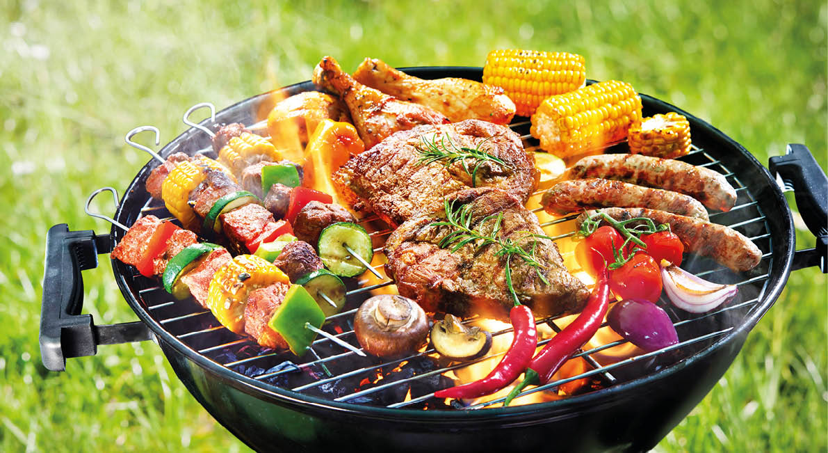 Assorted delicious grilled meat with vegetables on barbecue grill with smoke and flames in green grass