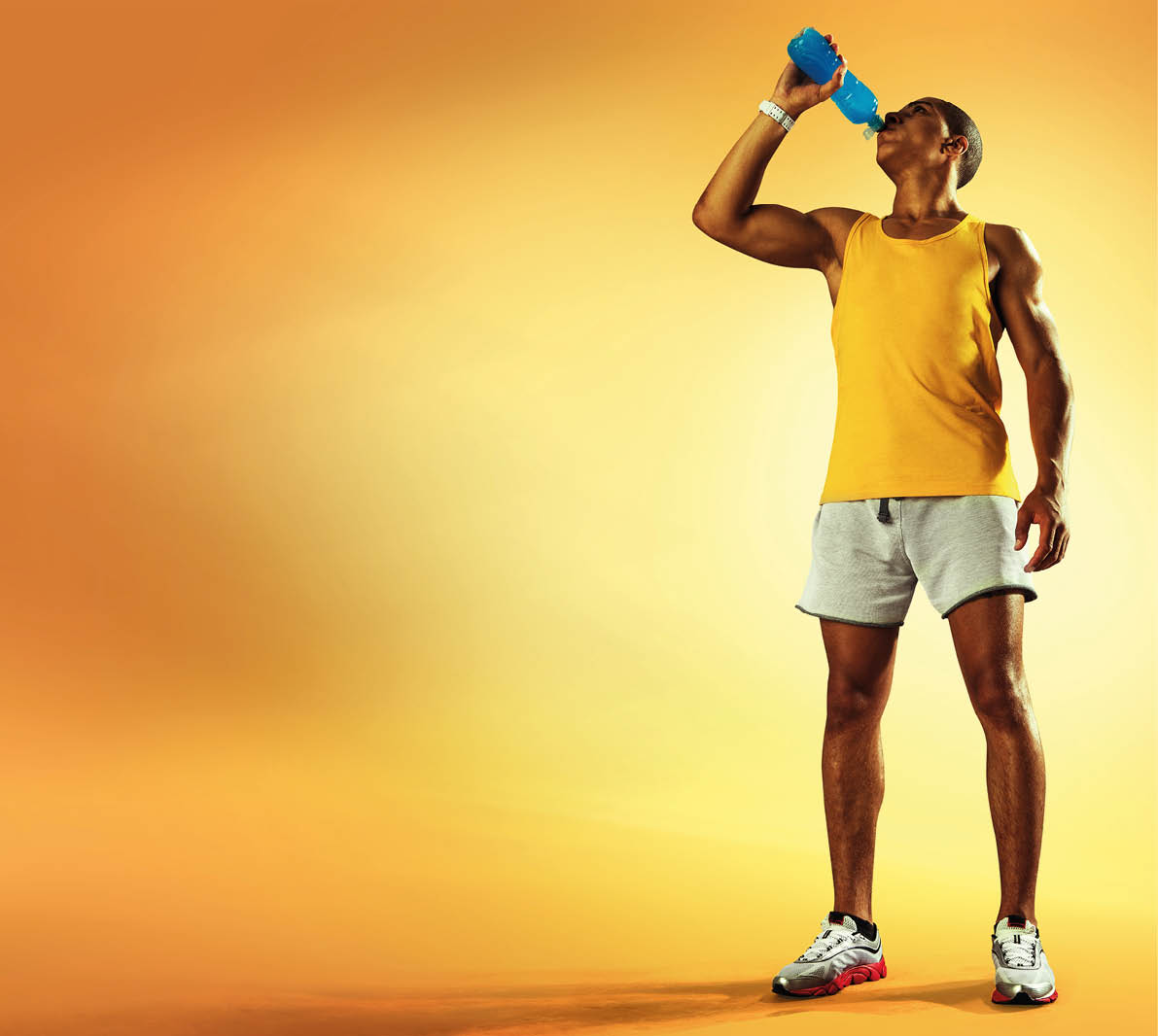 Young muscular build man drinking water of bottle after running, attractive athlete resting after workout outdoors, fitness and healthy lifestyle concept. Isolated on yellow