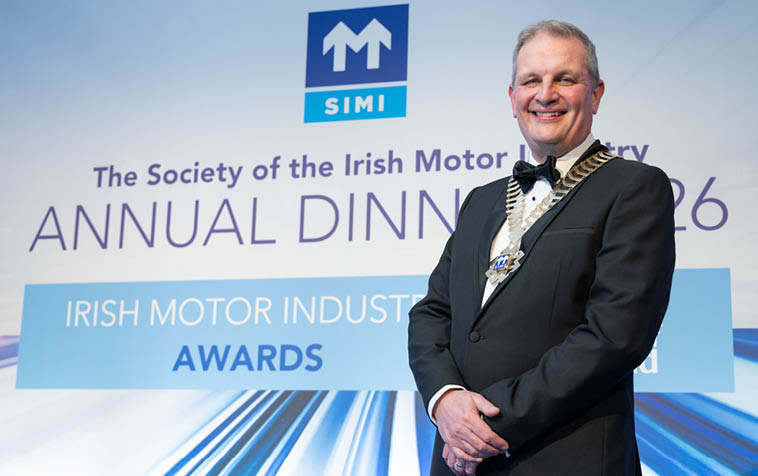A man in a suit and tie is standing in front of a sign for the Society of the Irish Motor Industry. AI generated content