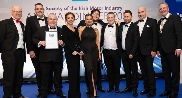 A group of people, including a woman, pose for a photo. They are wearing formal attire, with some of them wearing ties. The woman is holding an award, and the group appears to be celebrating a special occasion. AI generated content