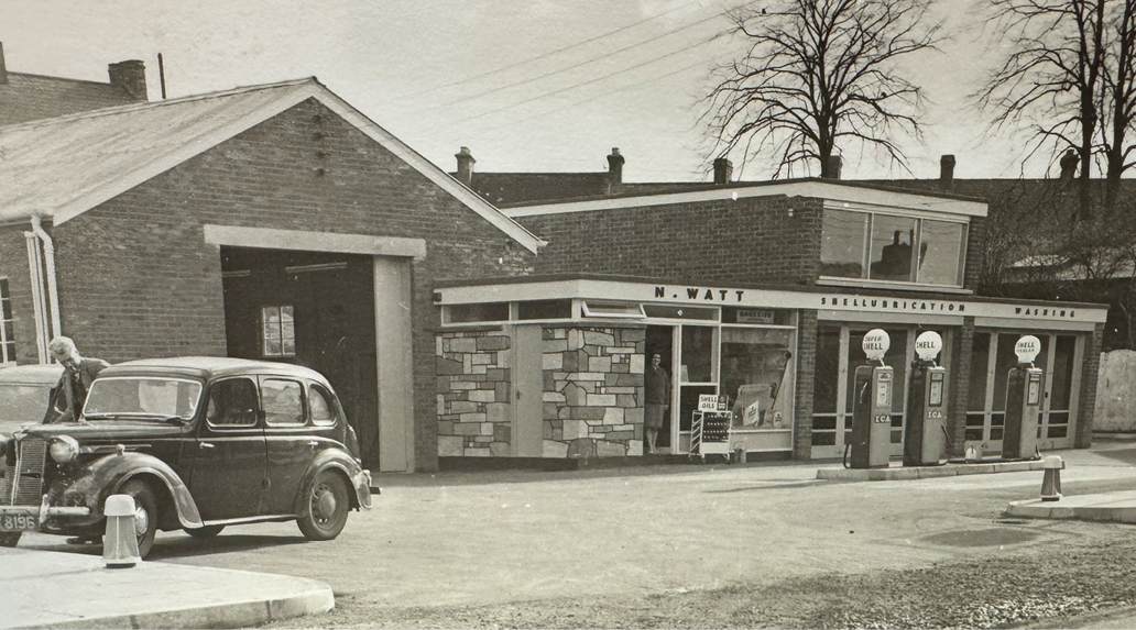An old car is parked in front of a building, which appears to be a gas station. AI generated content