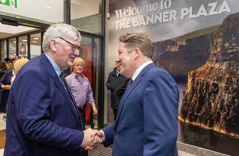 Two men shake hands in front of a sign that reads “Welcome to the Banner Plaza." AI generated content
