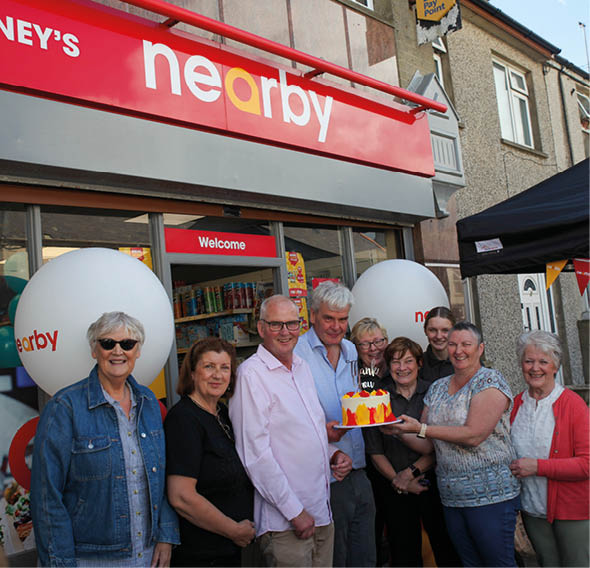 A group of people are standing in front of a store, posing for a picture. One of the women is holding a cake. AI generated content