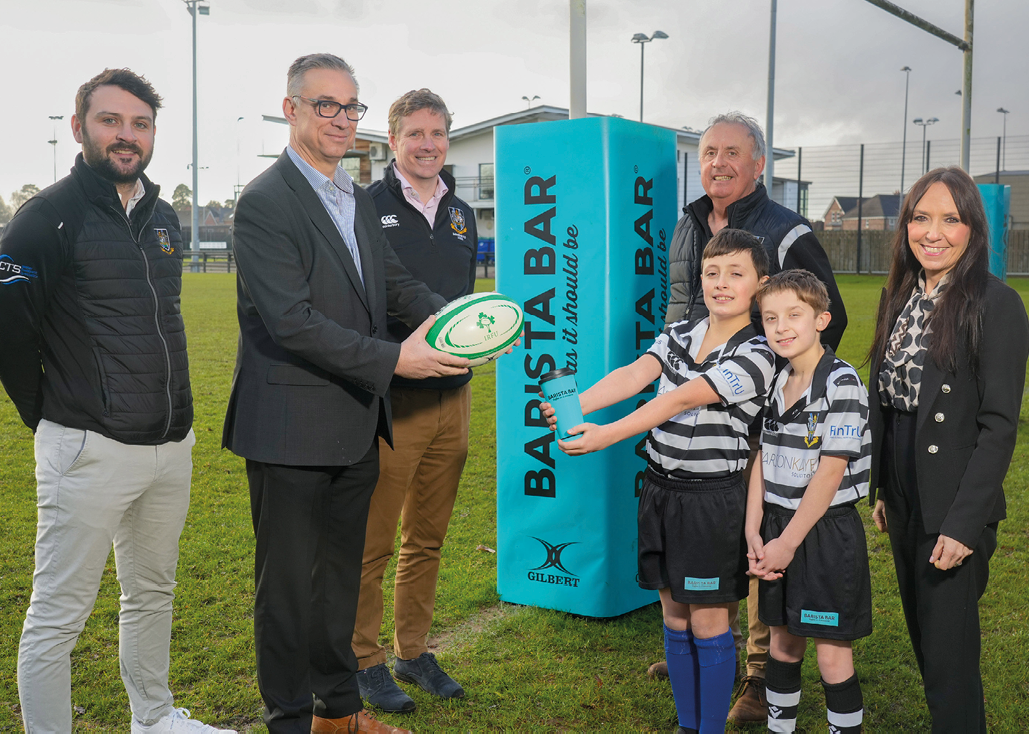 A group of people, including a man holding a rugby ball, pose for a photo in front of a blue sign. AI generated content
