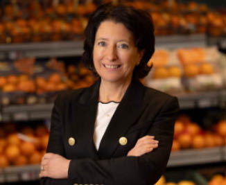 A woman in a black suit stands in front of a fruit display. AI generated content