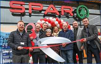 A group of people are standing in front of a store, holding a pair of scissors and a large red ribbon. They are posing for a photo, possibly to celebrate the opening of a new store or a special event. AI generated content
