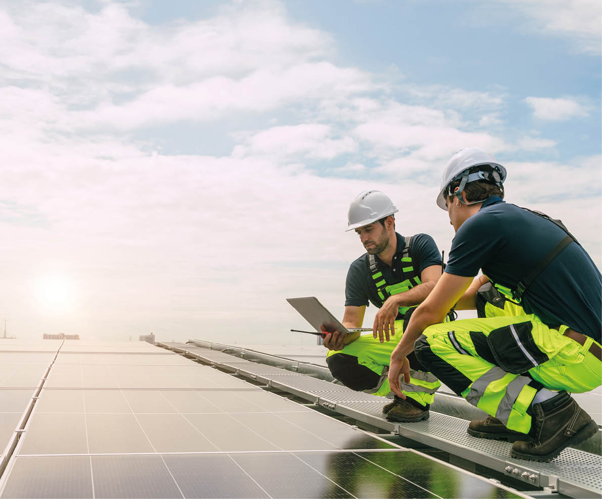 Two men wearing hard hats and safety vests are looking at a laptop. Description generated by AI