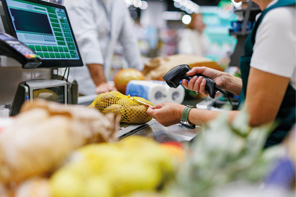 Supermarket cashier scanning potatoes at the checkout counter, processing groceries for a customer during a busy shopping day