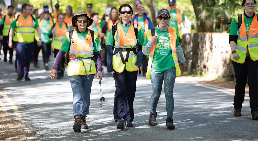 A group of people wearing neon green vests and walking down a road. Description generated by AI