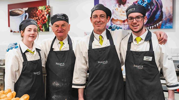 Four people wearing black aprons and white hats. Description generated by AI
