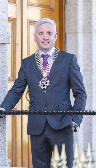 A man wearing a suit and tie with a gold chain around his neck. Description generated by AI