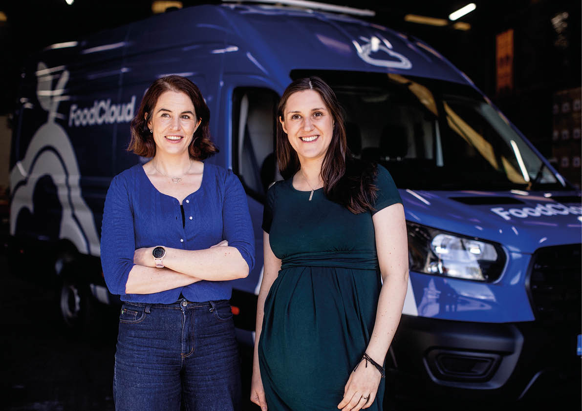 Two women standing in front of a blue truck. Description generated by AI