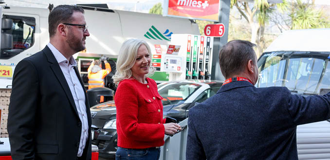 A man and a woman are standing in front of a gas station. Description generated by AI