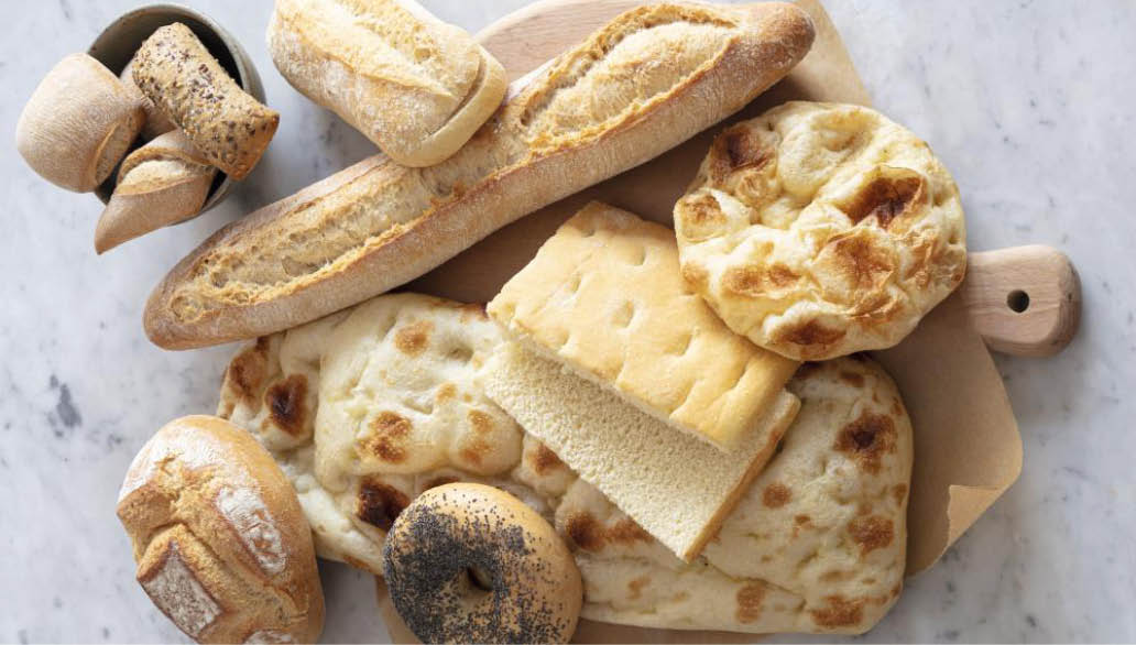A wooden cutting board with a variety of breads and pastries on it. Description generated by AI