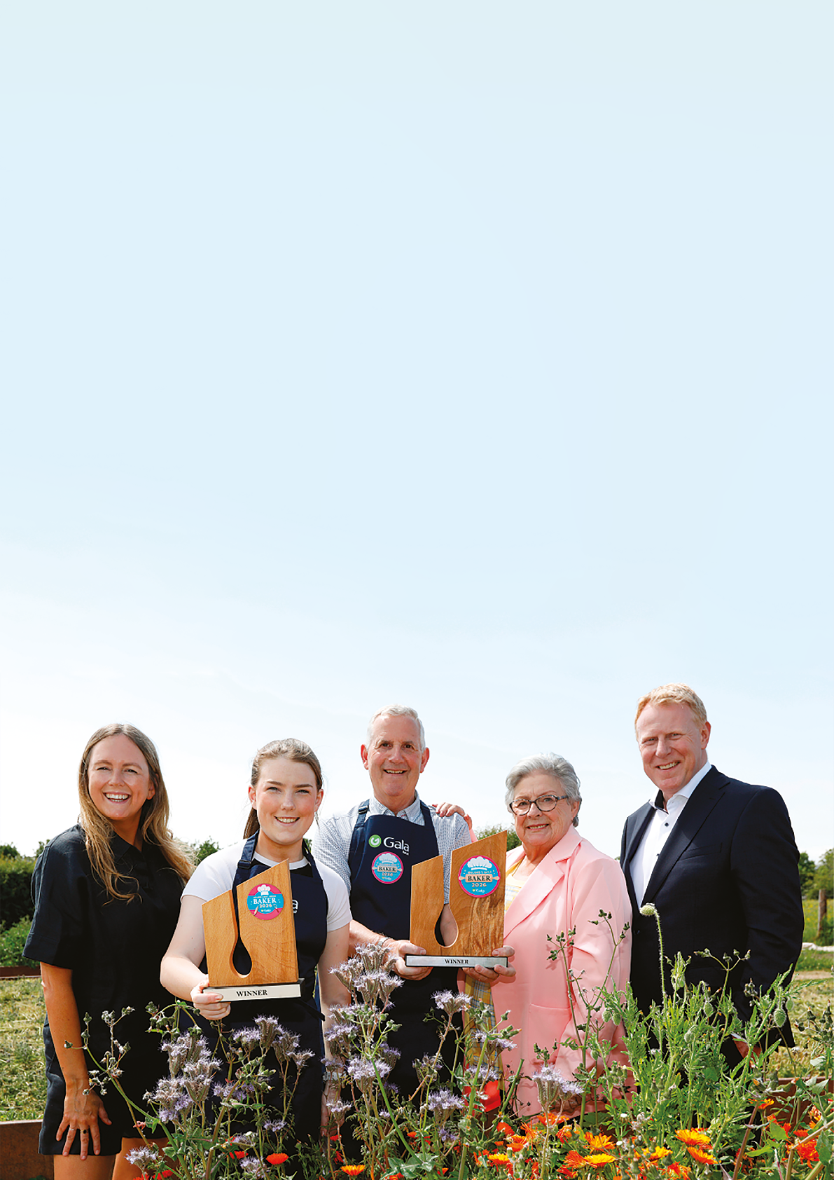 Four people are standing in front of a flower garden. Description generated by AI