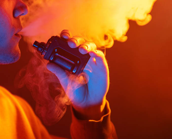 Vaping man exhales a cloud of steam, holding an electronic cigarette. Close-up.