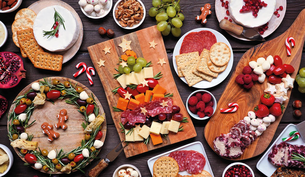 Christmas charcuterie table scene against a dark wood background. Assortment of cheese and meat appetizers. Christmas tree, wreath and candy cane arrangements.