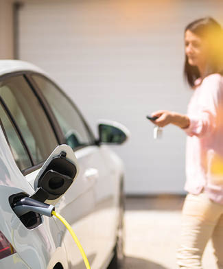 Close up of a electric car charger with female silhouette in the background, locking a car