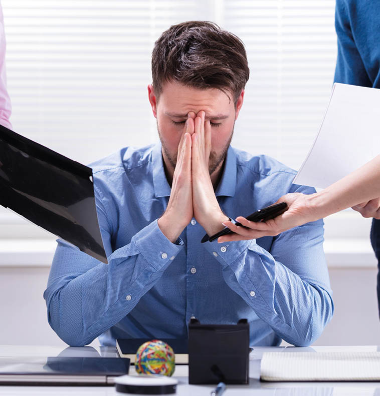 Stressed Businessman Sitting In Office Surrounded By Businesspeople