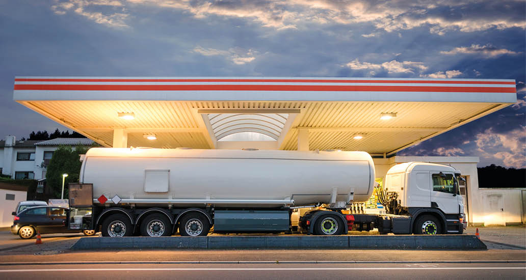 Tanker gas truck delivering fuel at service station against dramatic night sky