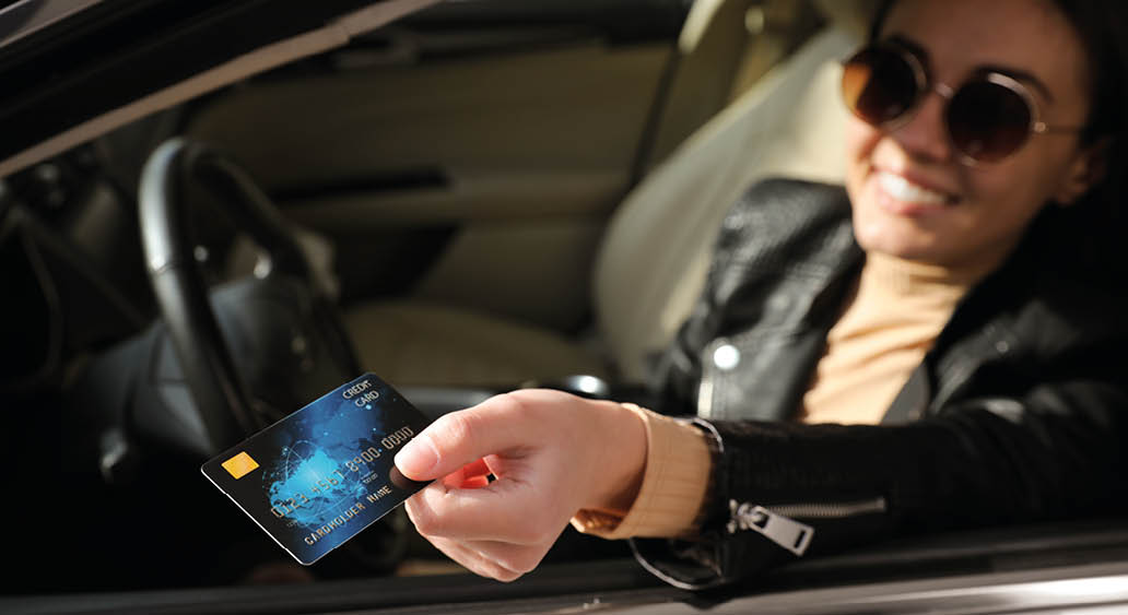 Woman sitting in car and giving credit card at gas station, focus on hand