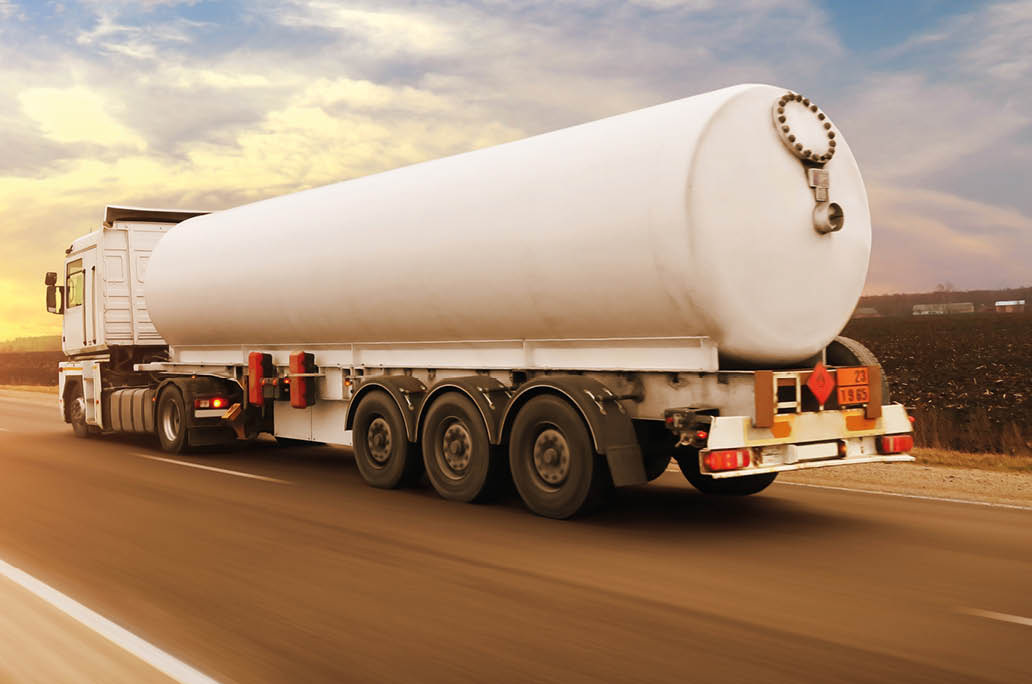 Big white fuel tanker truck shipping fuel on the countryside road in motion against a night sky with a sunset