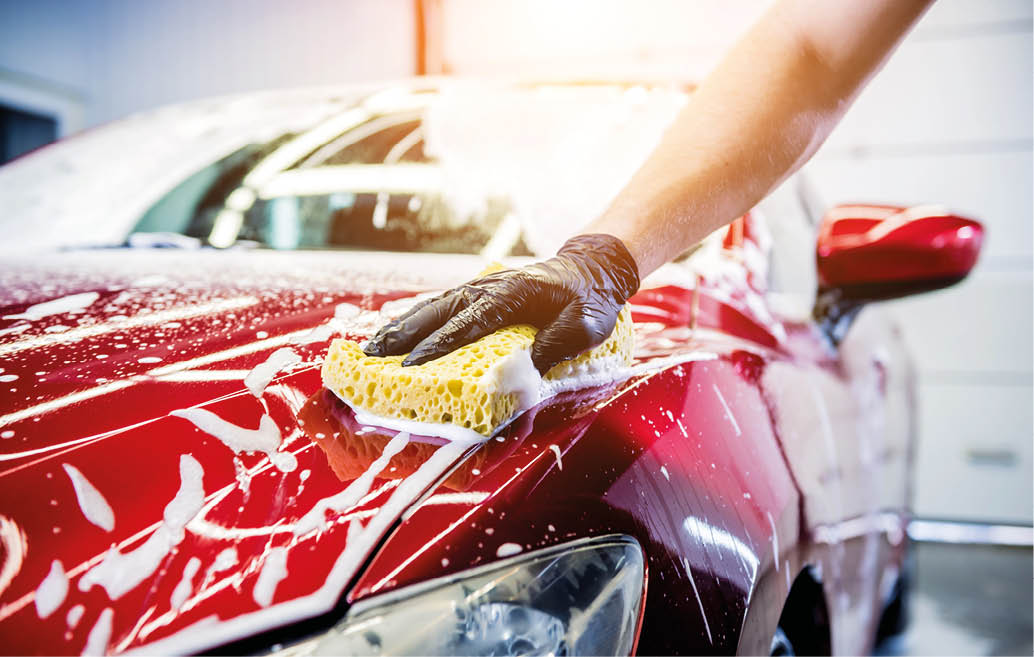 Worker washing red car with sponge on a car wash