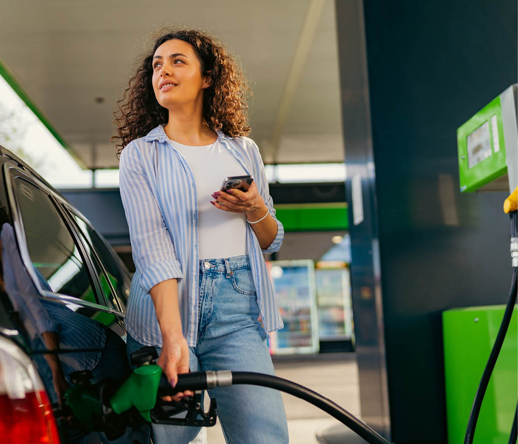 A young beautiful woman does not follow the safety rules and uses the phone while filling her car gas tank