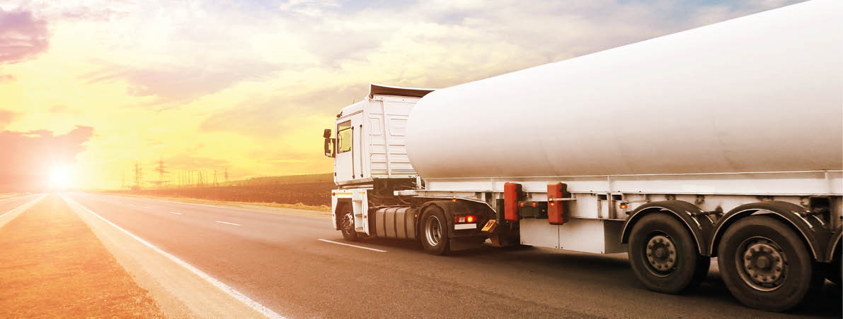 Big metal fuel tanker truck shipping fuel on the countryside road against a night sky with a sunset