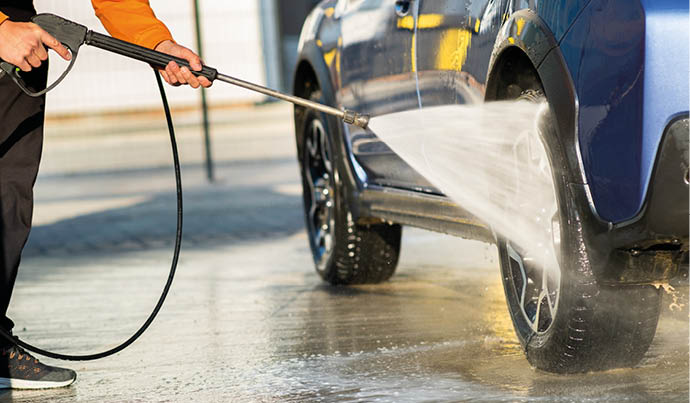 Closeup of male driver washing his car with contactless high pressure water jet in self service car wash.