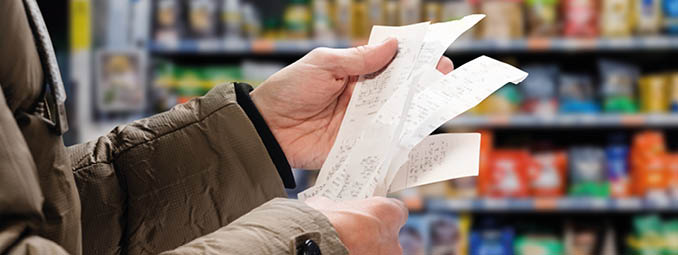 Minded man viewing receipts in supermarket and tracking prices