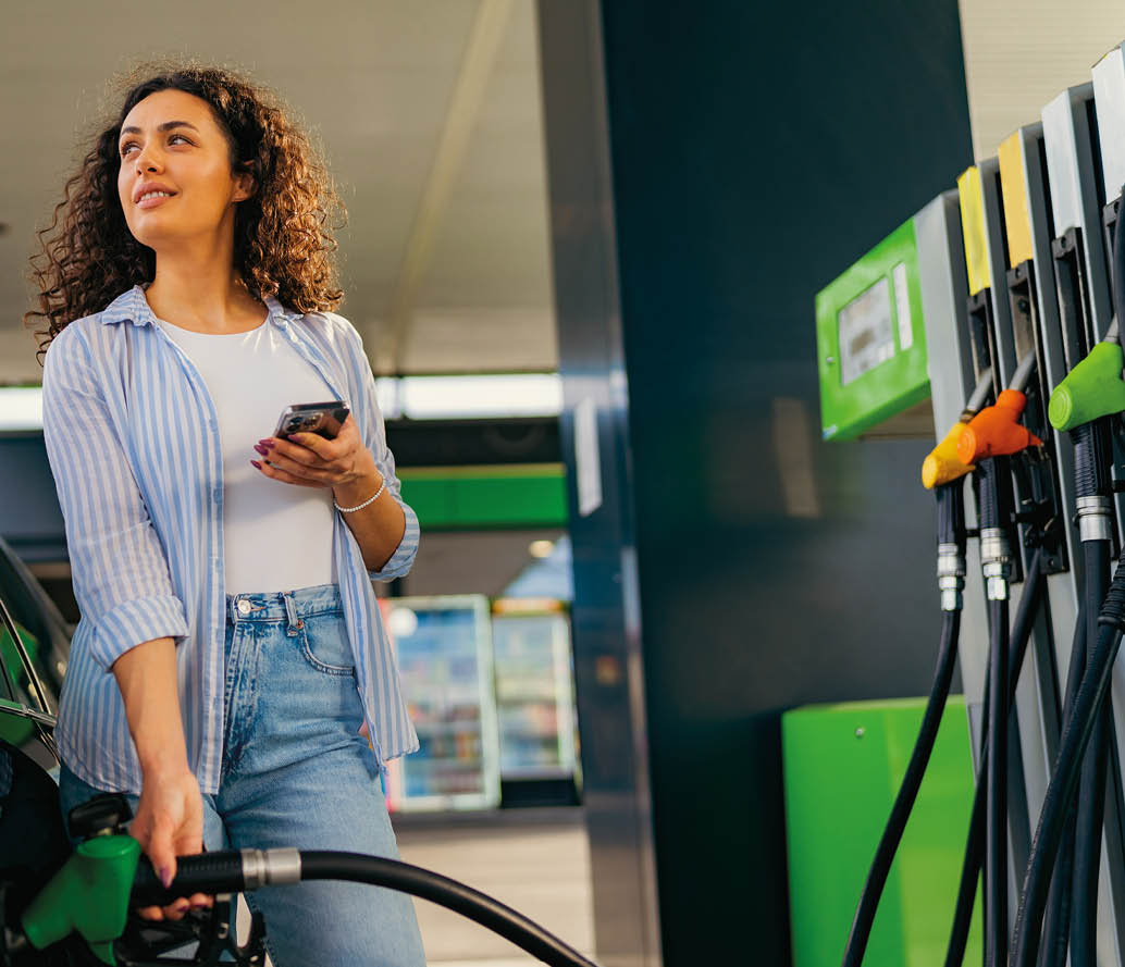 A young beautiful woman does not follow the safety rules and uses the phone while filling her car gas tank