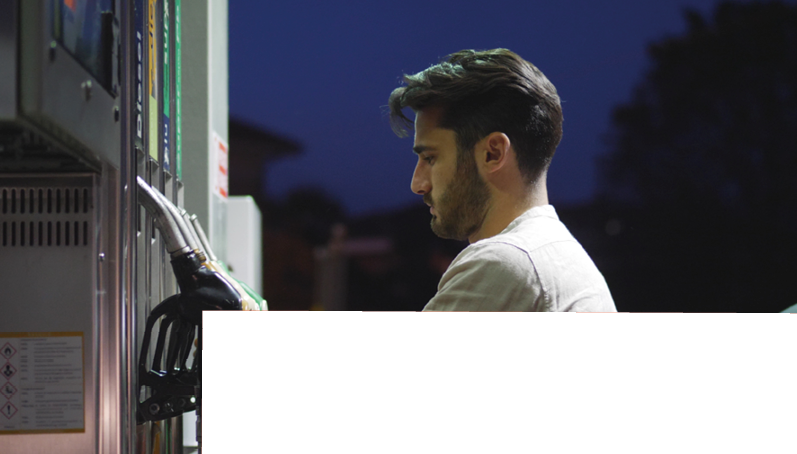 Young man fueling his car at gas station, using the pump nozzle. Late at night