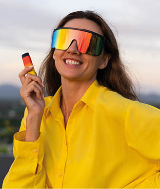 Stylish fit fashion women in bright yellow shirt trendy shield visor rainbow sunglasses posing at rooftop terrace tropical view sunset smoking vape pod enjoying puffs