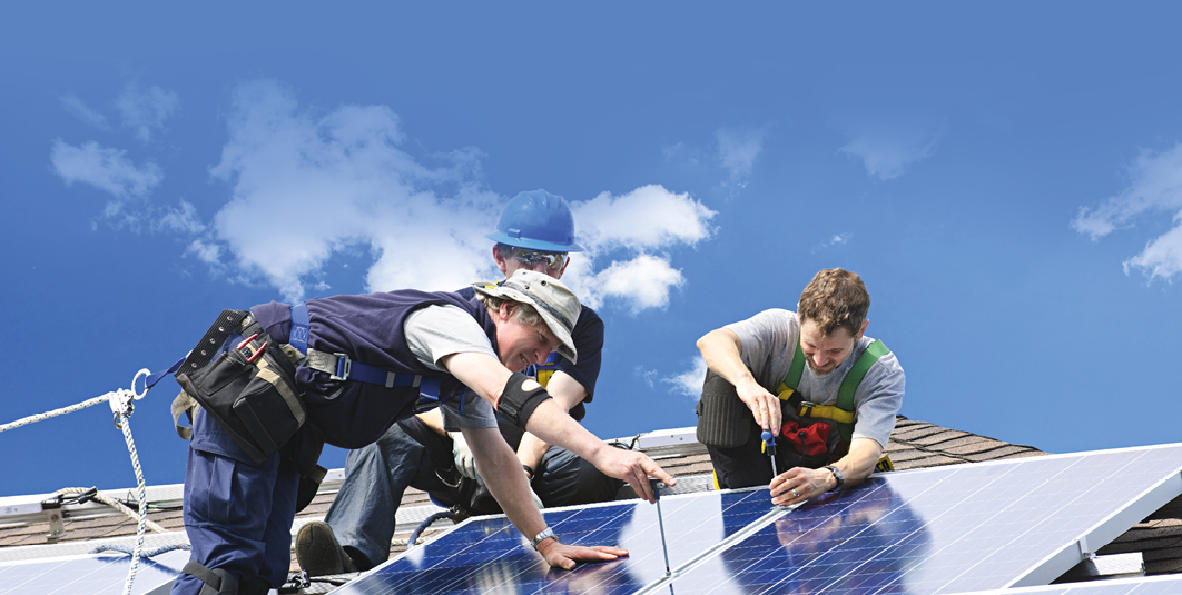 Workers installing alternative energy photovoltaic solar panels on roof