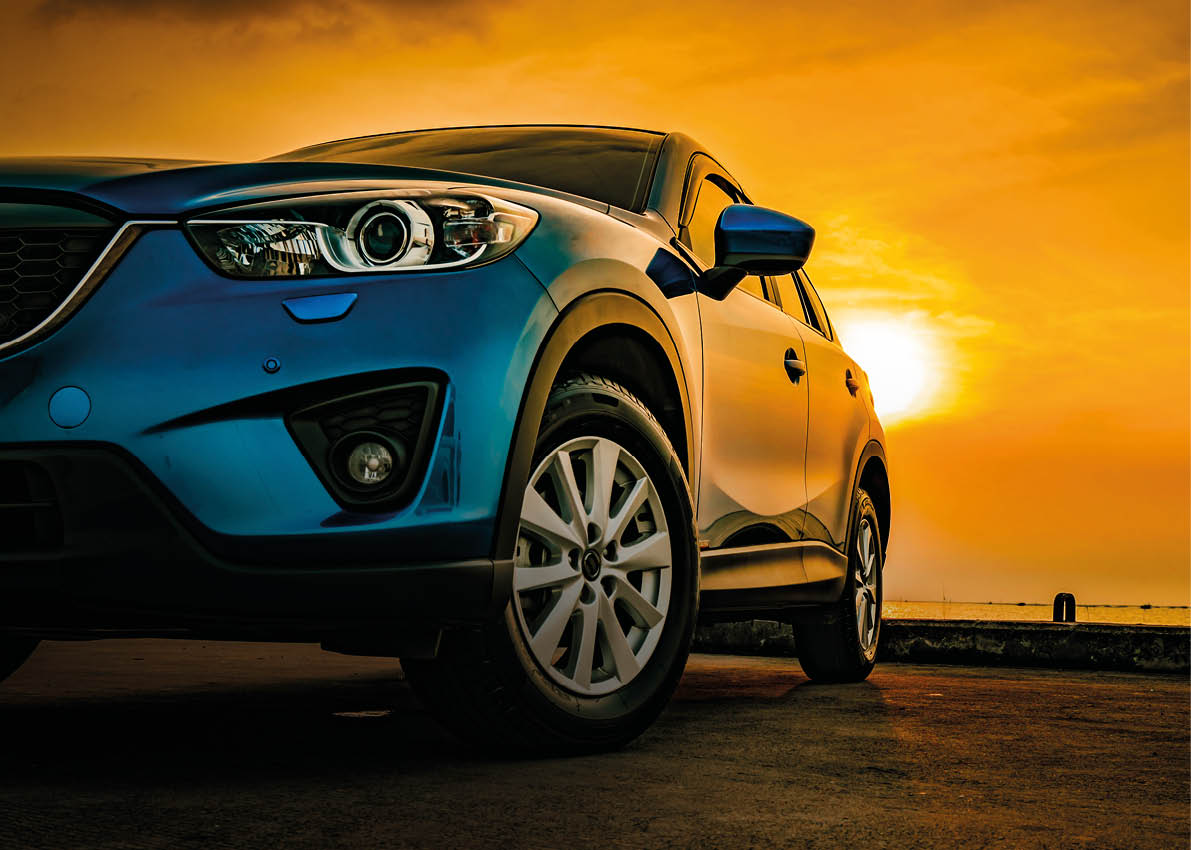 Blue compact SUV car with sport and modern design parked on concrete road by the sea at sunset. Environmentally friendly technology. Business success concept.