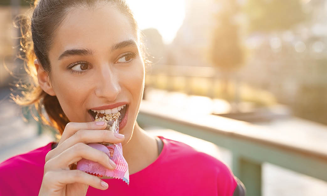 Athletic woman eating a protein bar  Closeup face of young sporty woman resting while biting a nutritive bar  Fitness beautiful woman eating a energy snack outdoor 